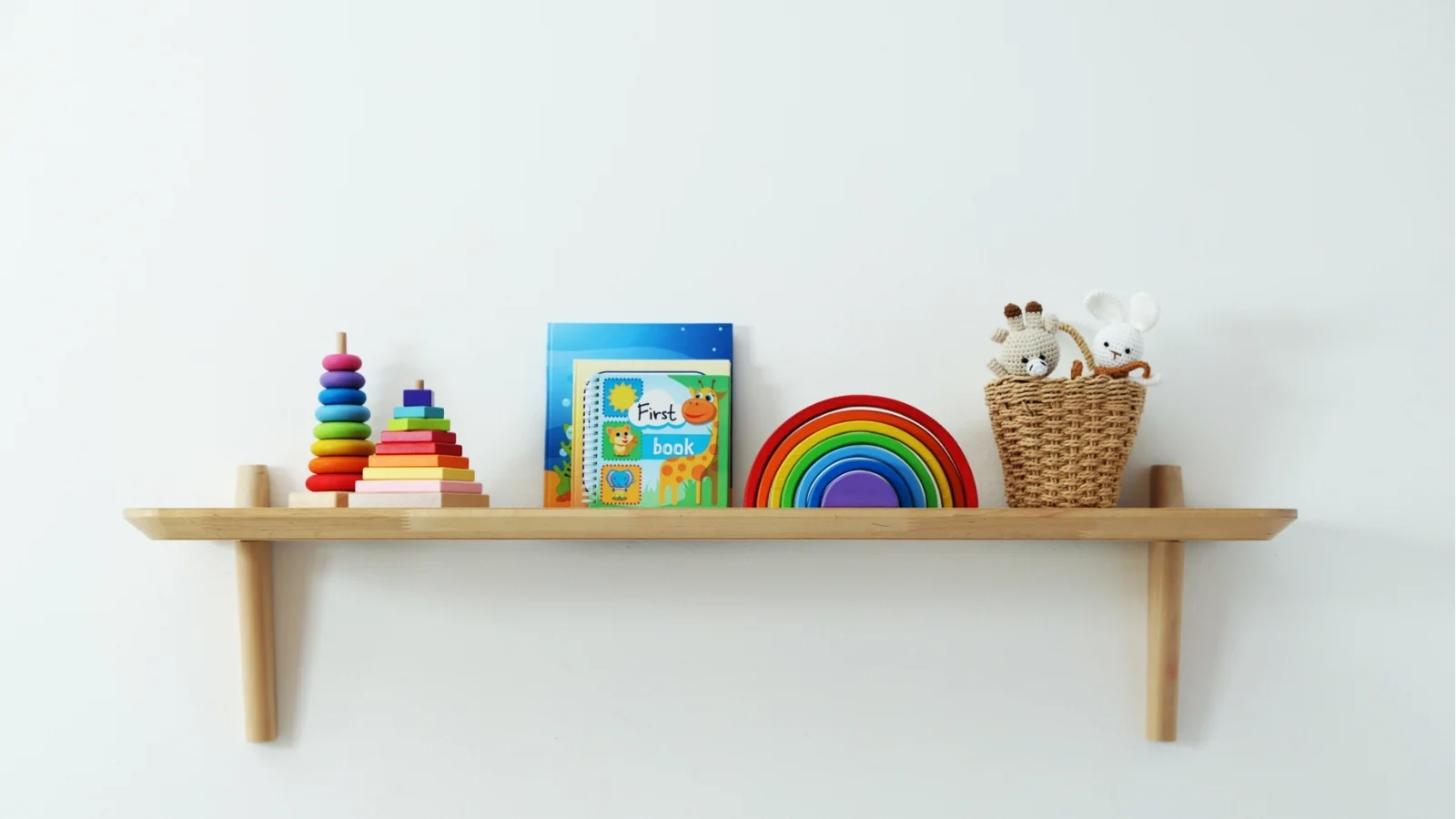 Montessori vs Waldorf toys on one simple shelf: ring stackers, a wooden rainbow, a board book and a basket of soft toys