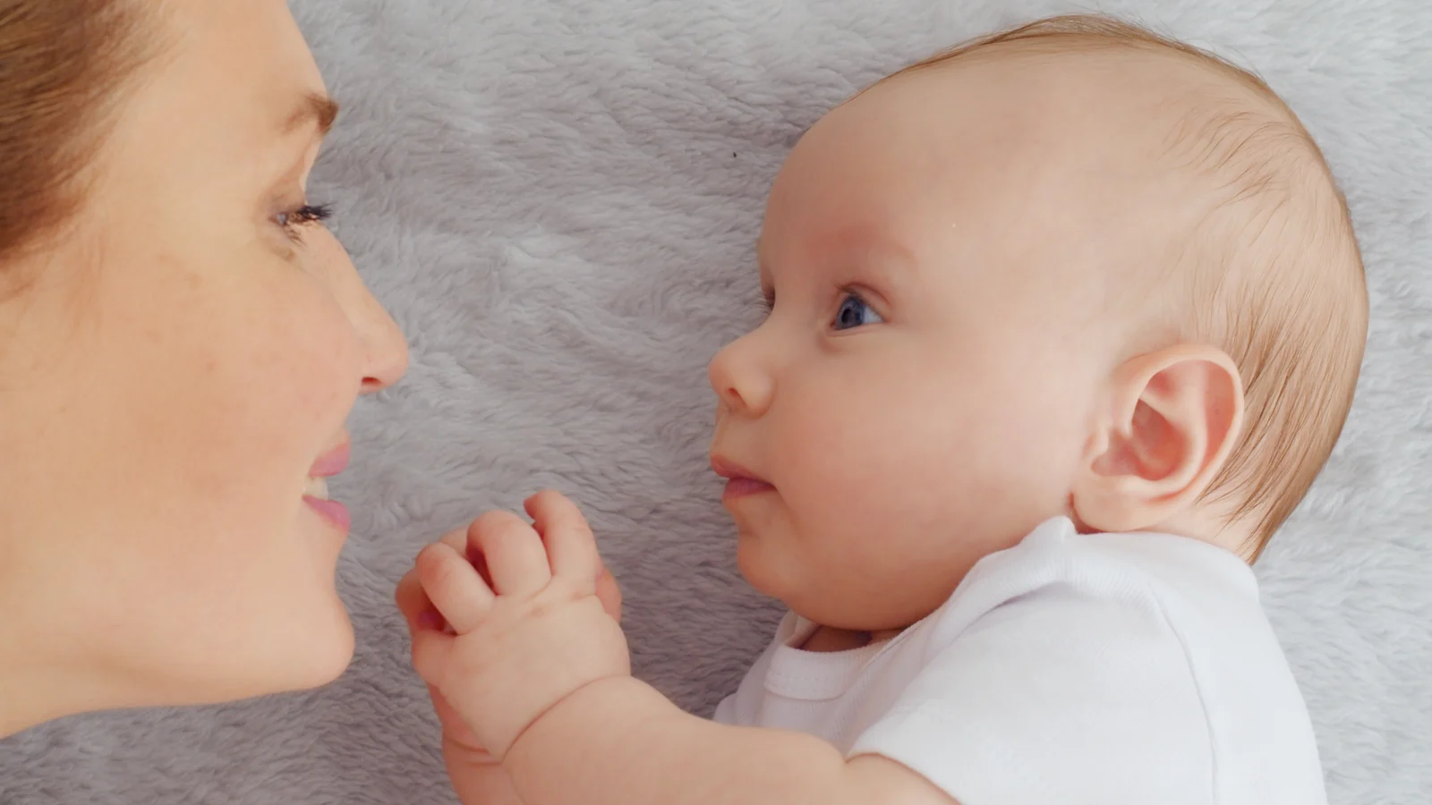 Baby lying face to face with a parent, the two gazing at each other