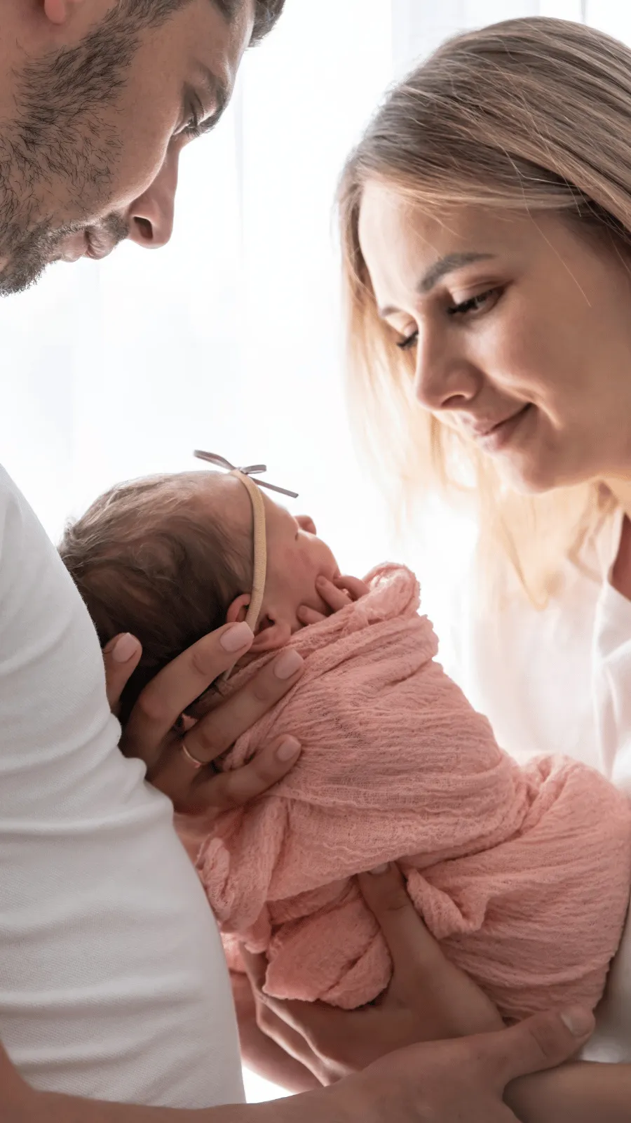 Newborn baby held close in a parent's arms, looking up at the parent's face