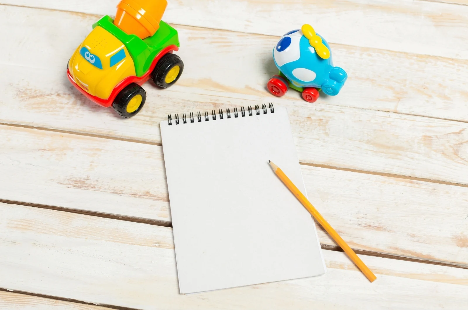 Blank spiral notepad and pencil on a wooden floor beside two toy cars
