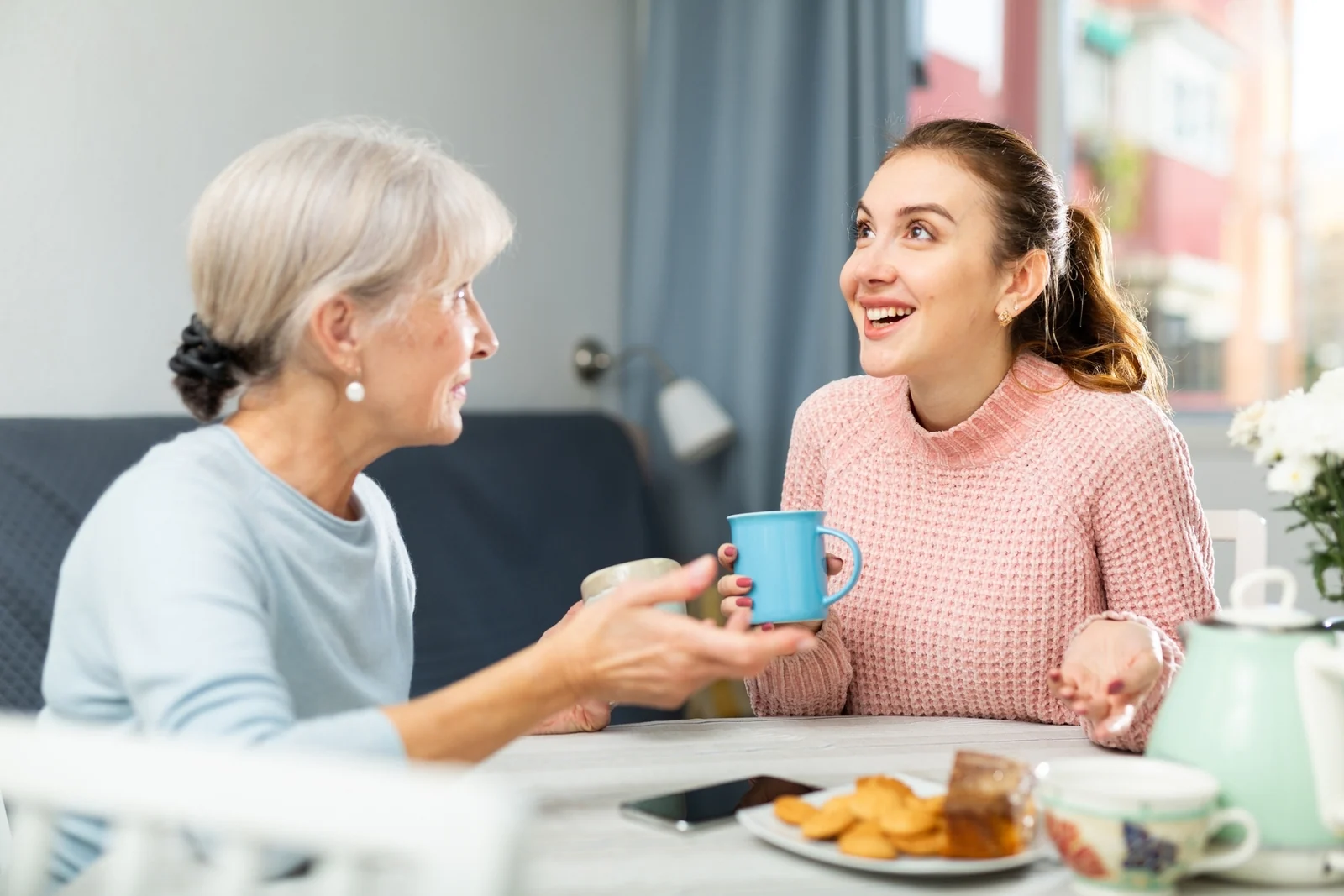 Older woman and younger woman chatting and smiling over coffee and snacks at a table