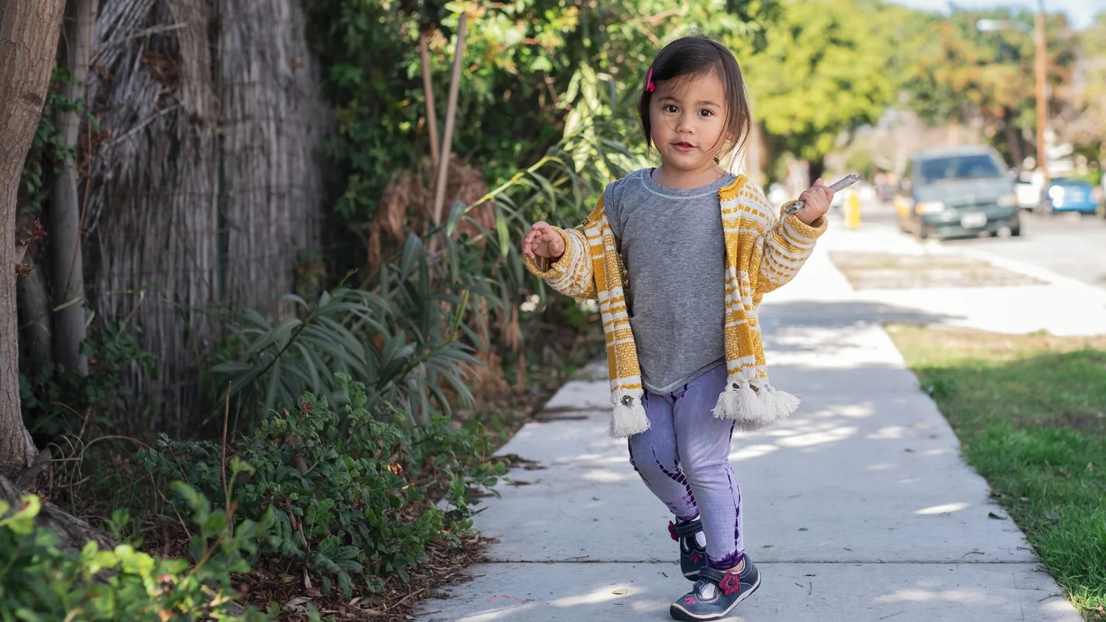Toddler walking along a sunny neighborhood sidewalk, one of the easiest outdoor activities for toddlers