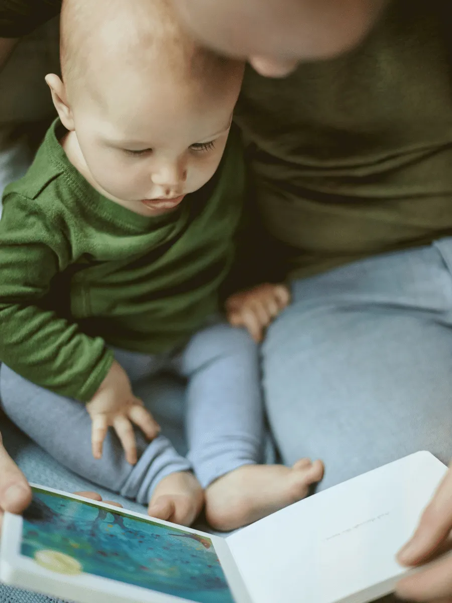 Parent holding a baby on their lap, pointing at a picture in a board book