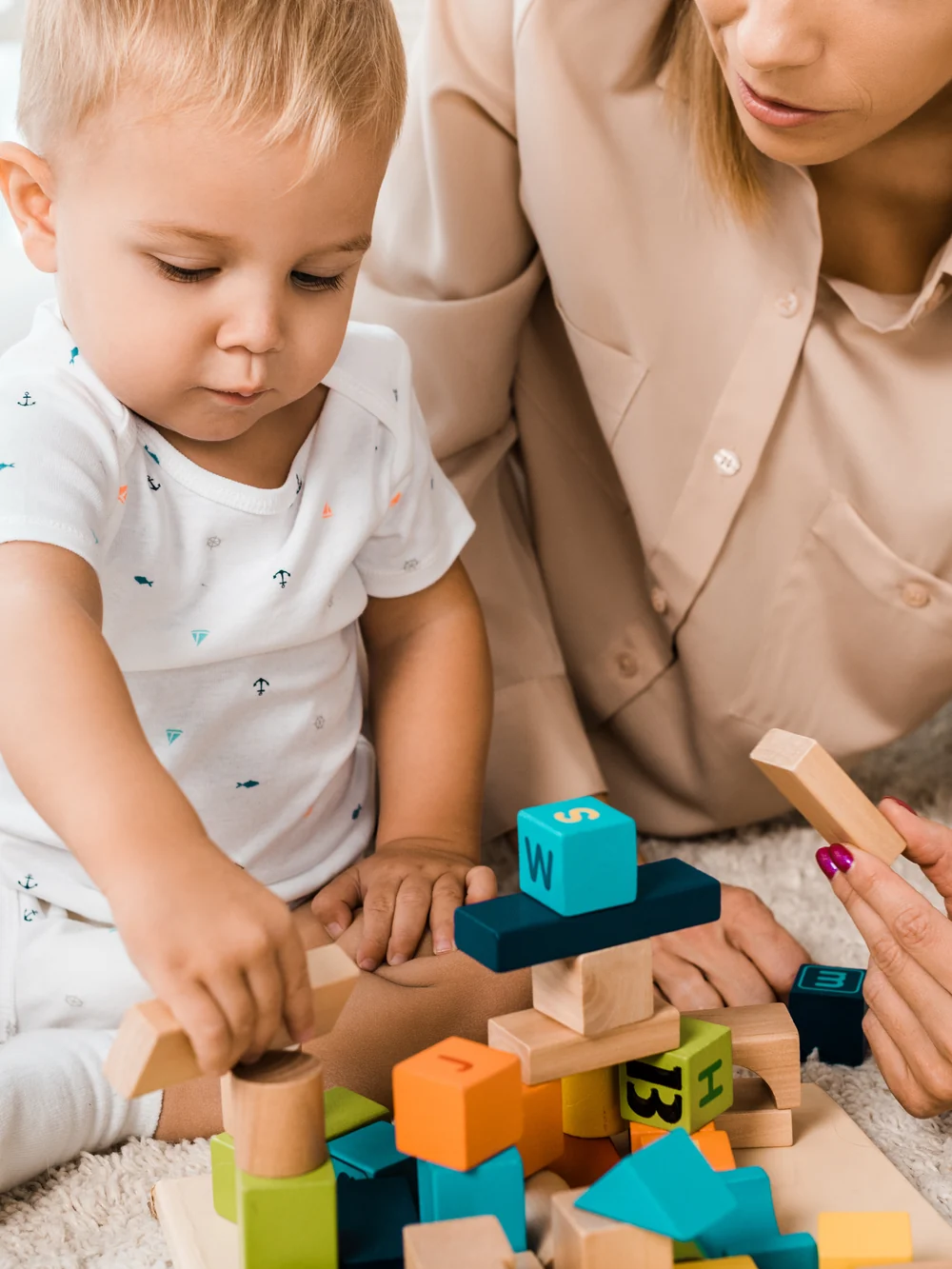 A parent and a toddler build with colorful wooden blocks together on a rug