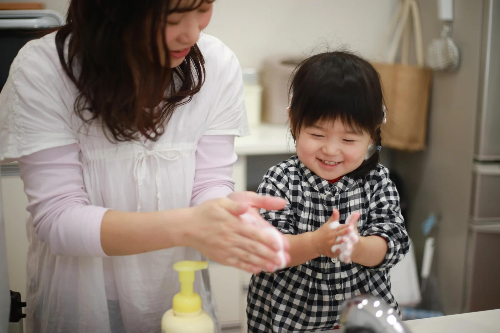 Parent and toddler lathering their hands with soap together at a kitchen sink