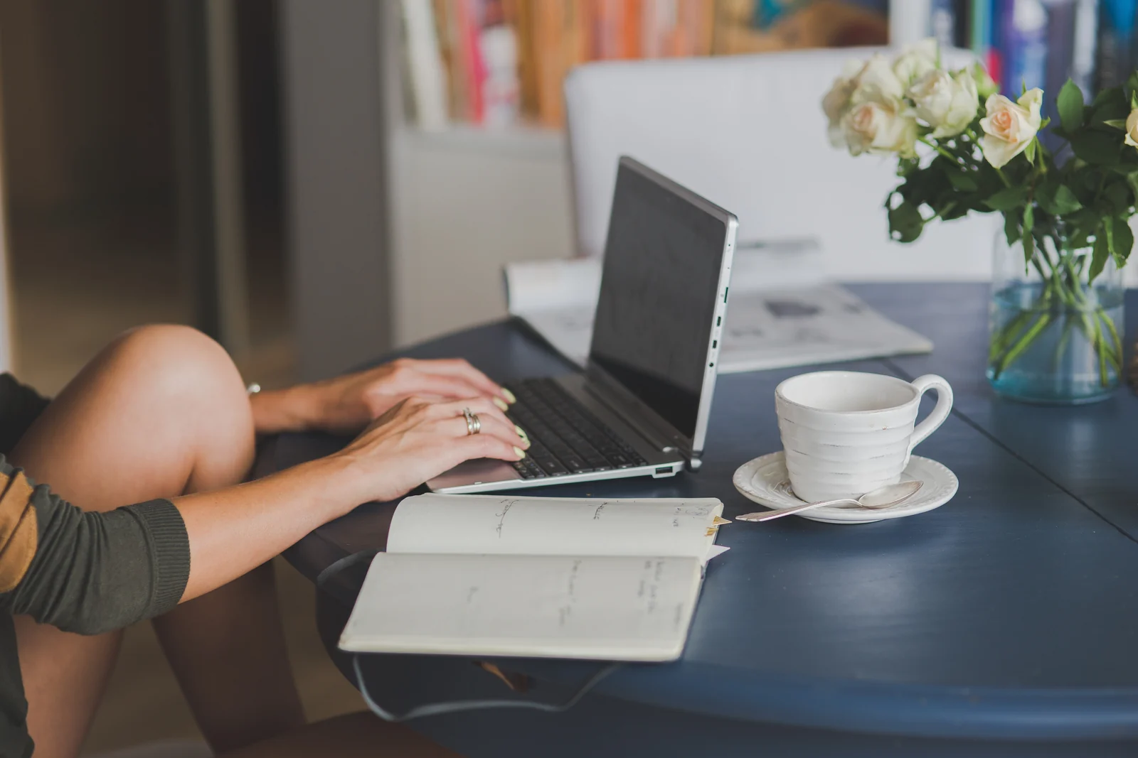 A parent sits at a kitchen table with a laptop and a notebook, working on a family budget