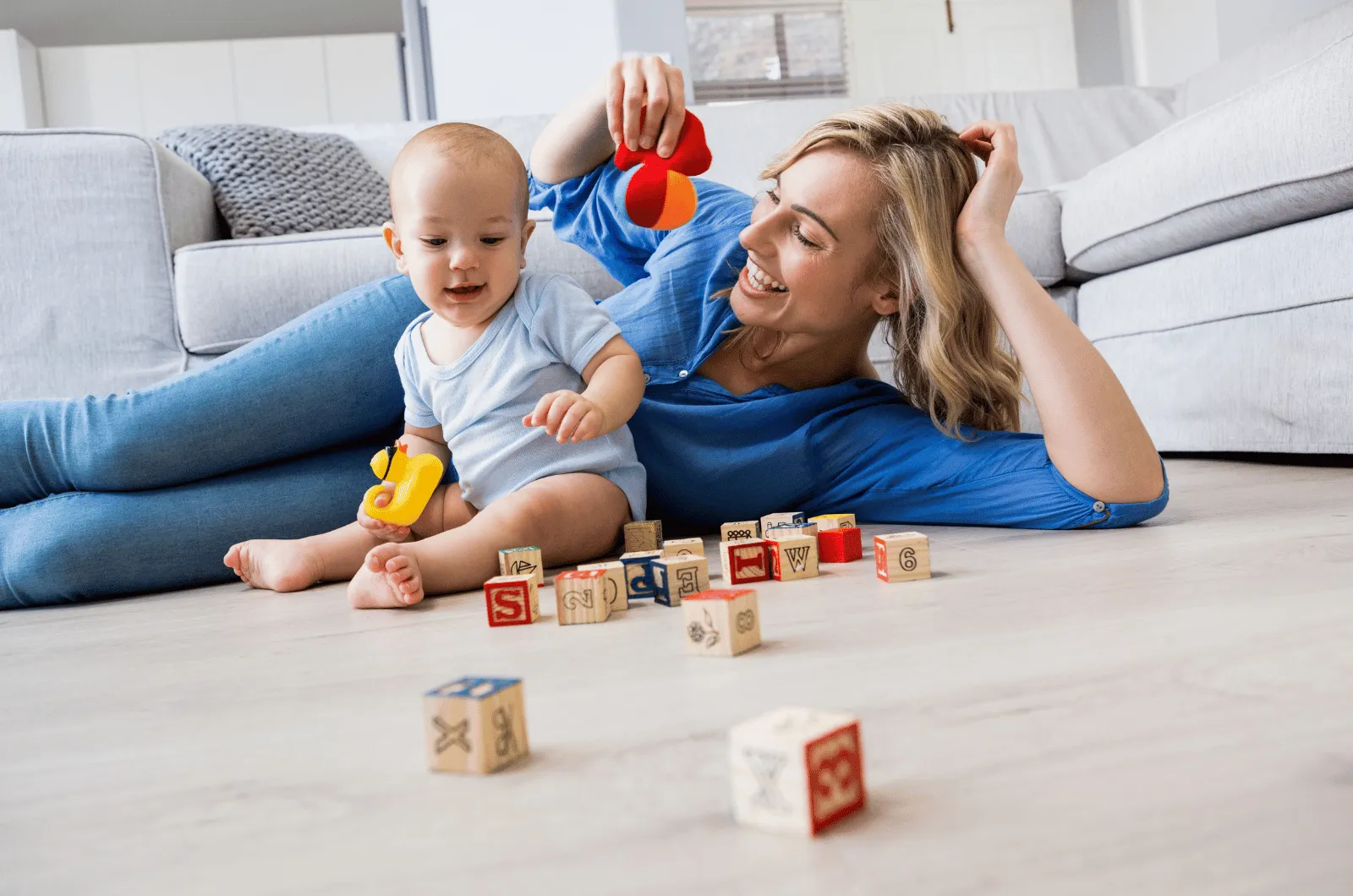 Parent sitting on the floor at a baby's eye level, quietly watching the baby play with a wooden toy