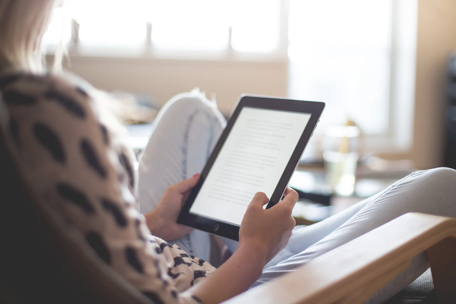 E-reader resting on a knit blanket next to a mug of tea