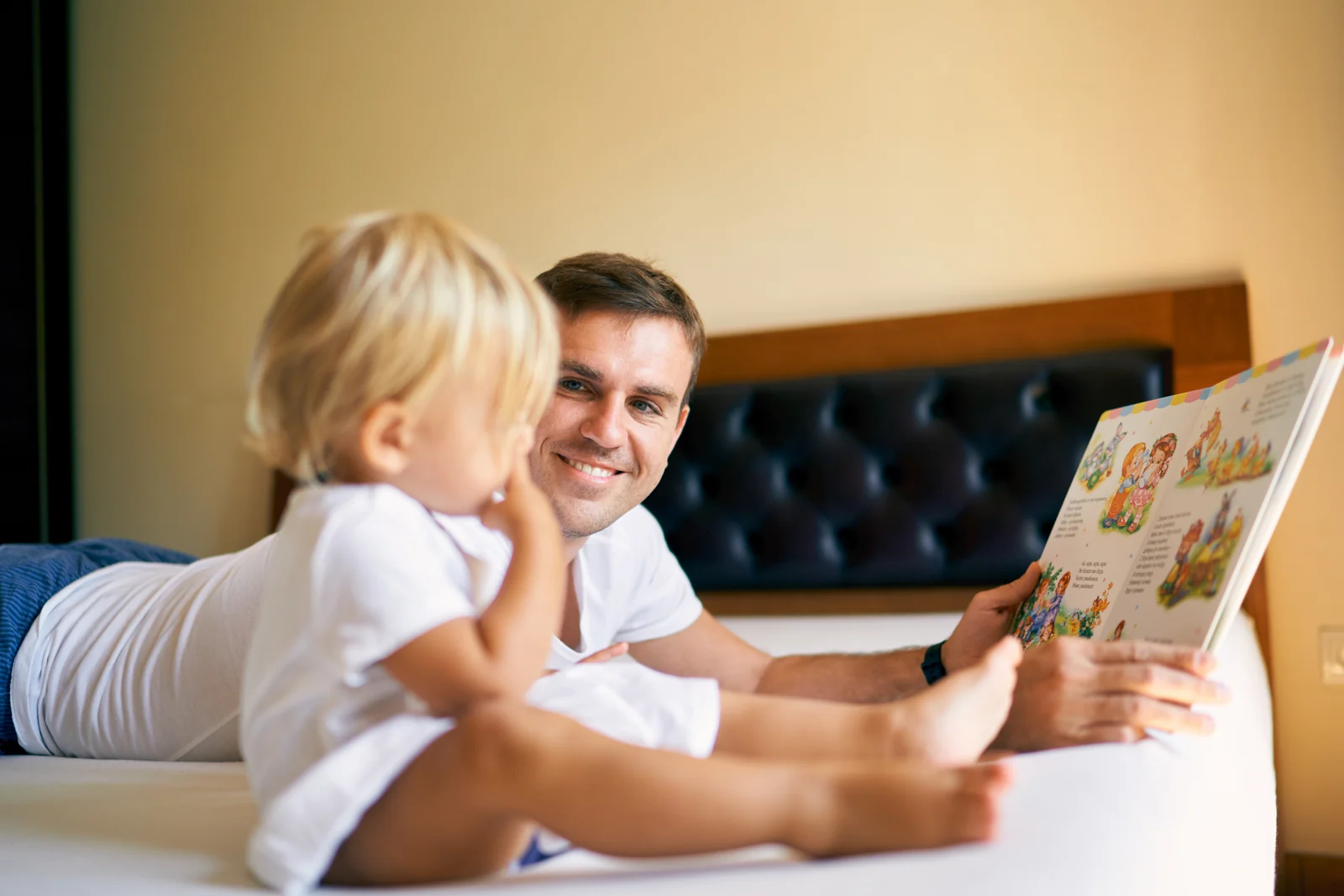 A parent reads a picture book to a toddler sitting on their lap