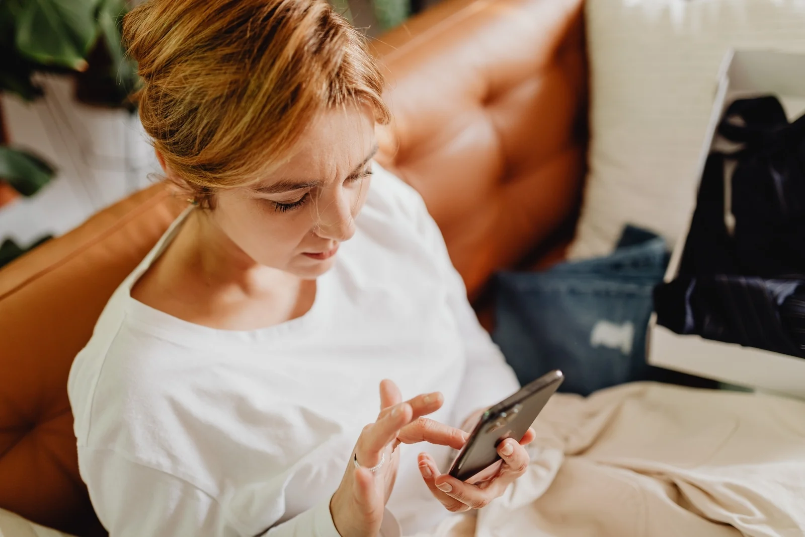 A parent sits on a couch in a dim living room at night, scrolling on a phone