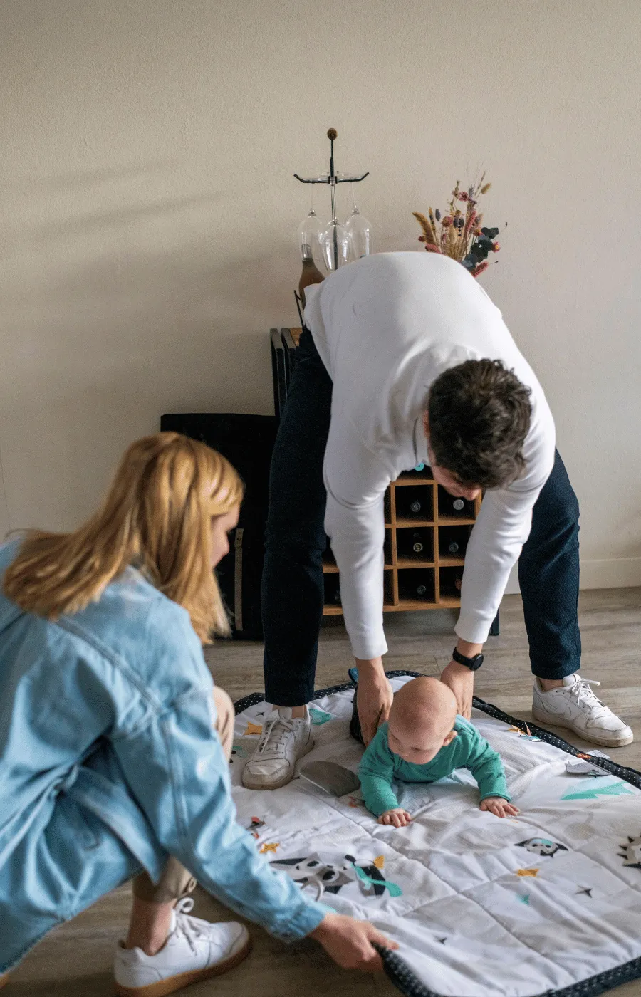 Parent leaning over a baby on a changing pad on the floor, talking to them face to face