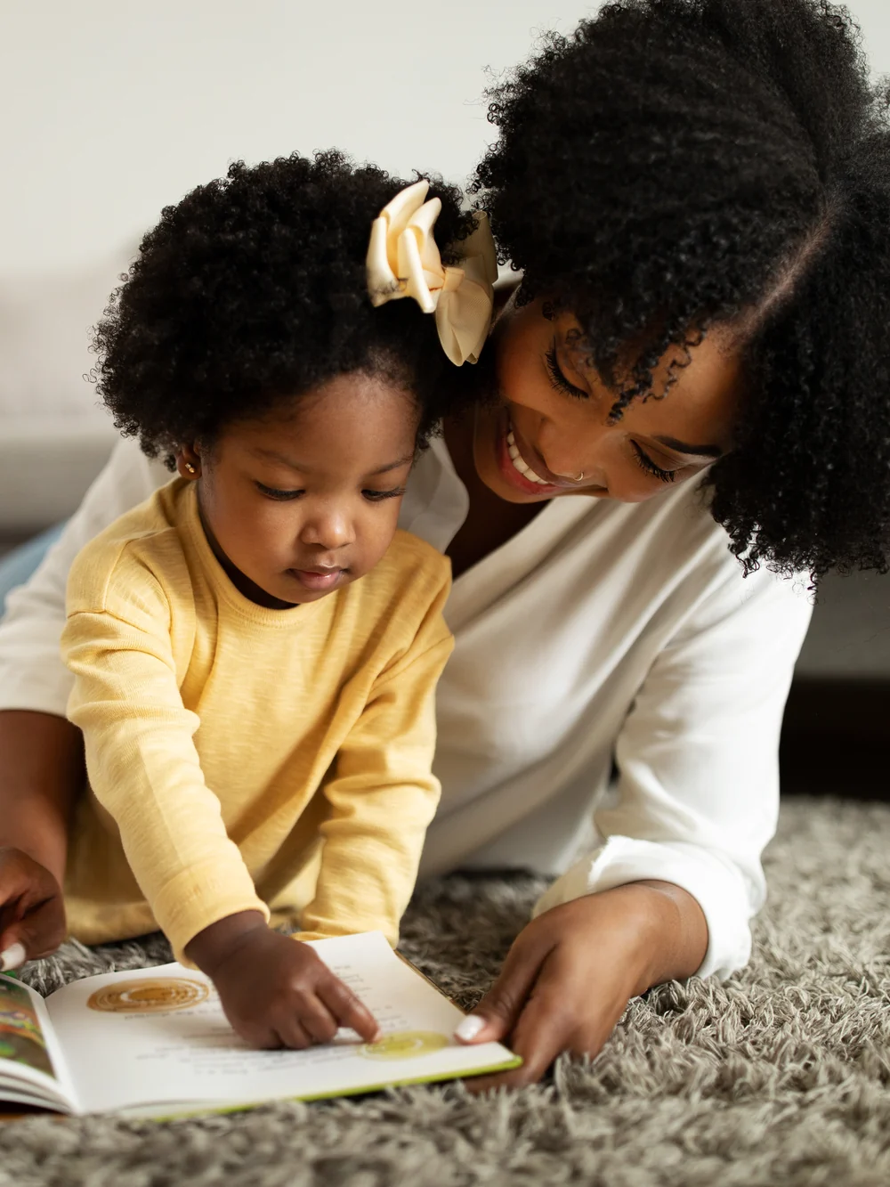 A parent and toddler lie on a soft rug looking at an open picture book together