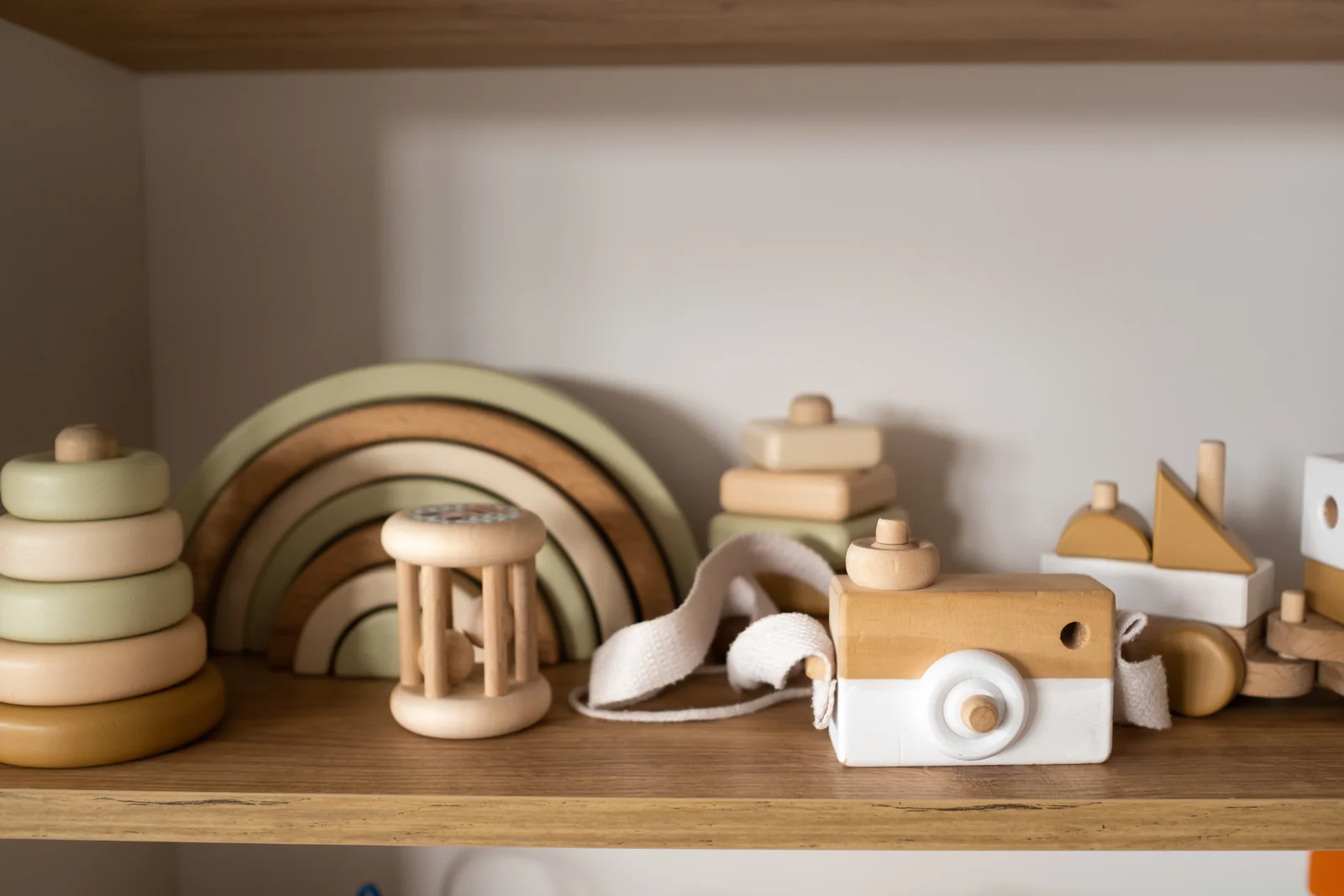 A shelf with a pastel wooden rainbow, ring stacker, rattle, toy camera and stacking blocks