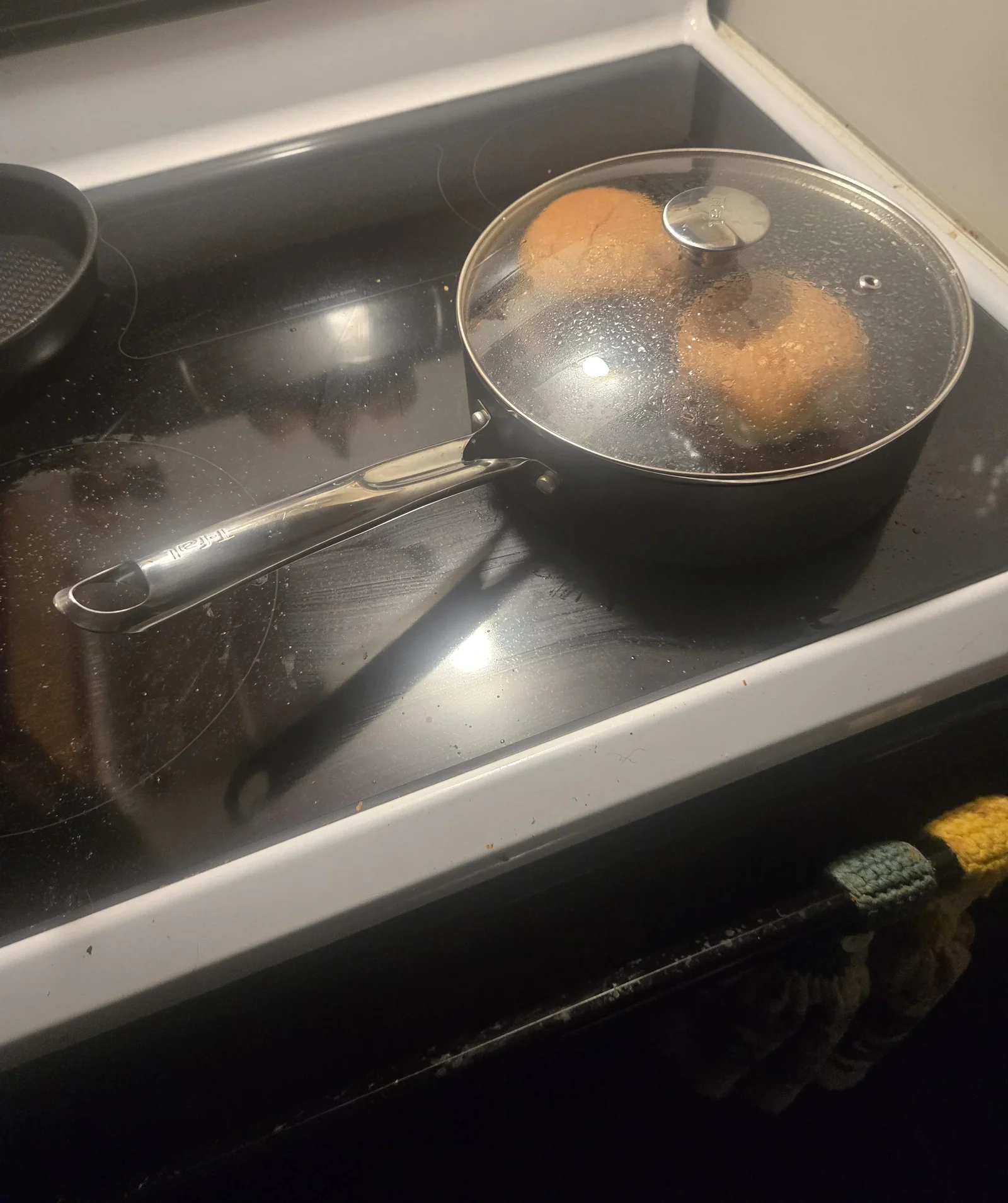 A saucepan with a glass lid on a stove burner, its handle turned in over the stovetop, not out past the front edge