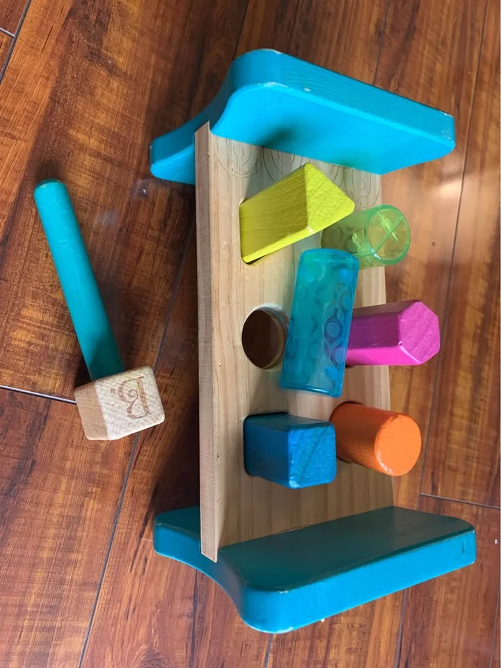 Wooden pounding bench with colorful pegs and a teal mallet resting on a hardwood floor