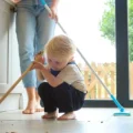Toddler with a small broom on a kitchen floor while a parent cleans behind them: practical life activities for Montessori