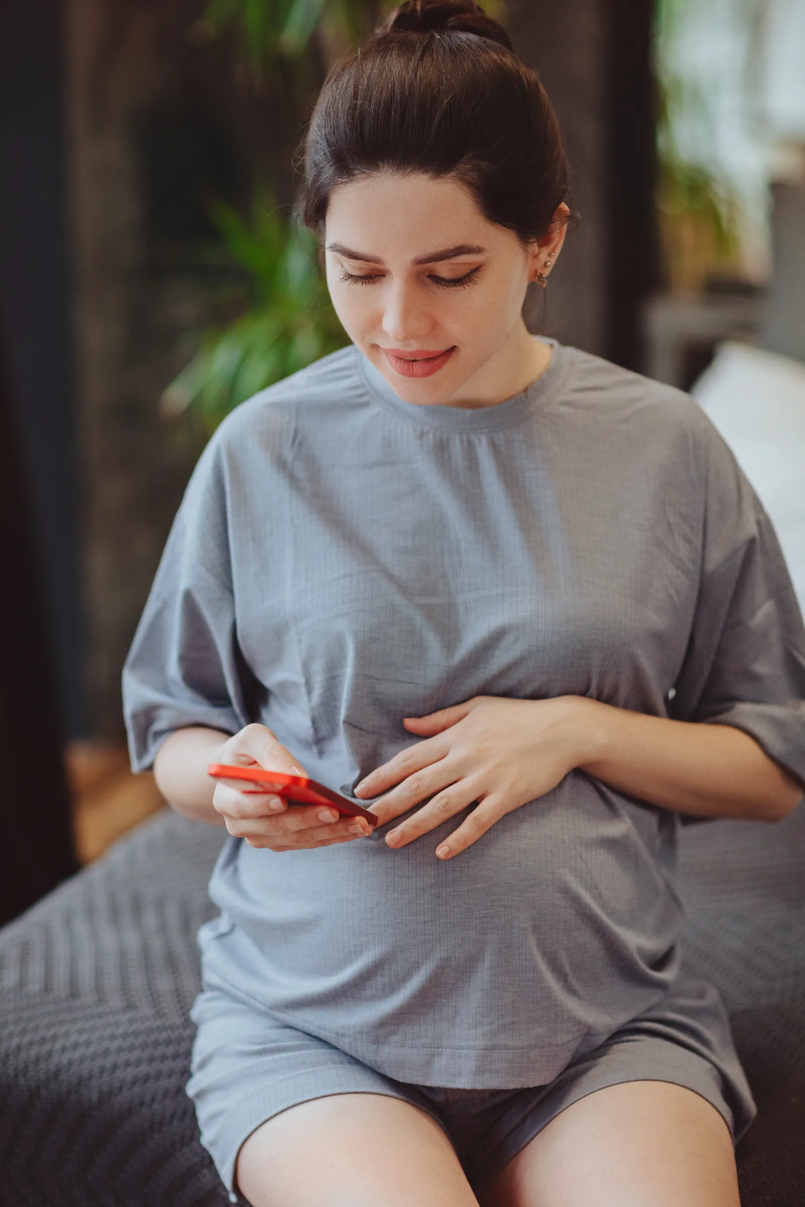 Pregnant person resting on a couch in the evening, scrolling on a phone