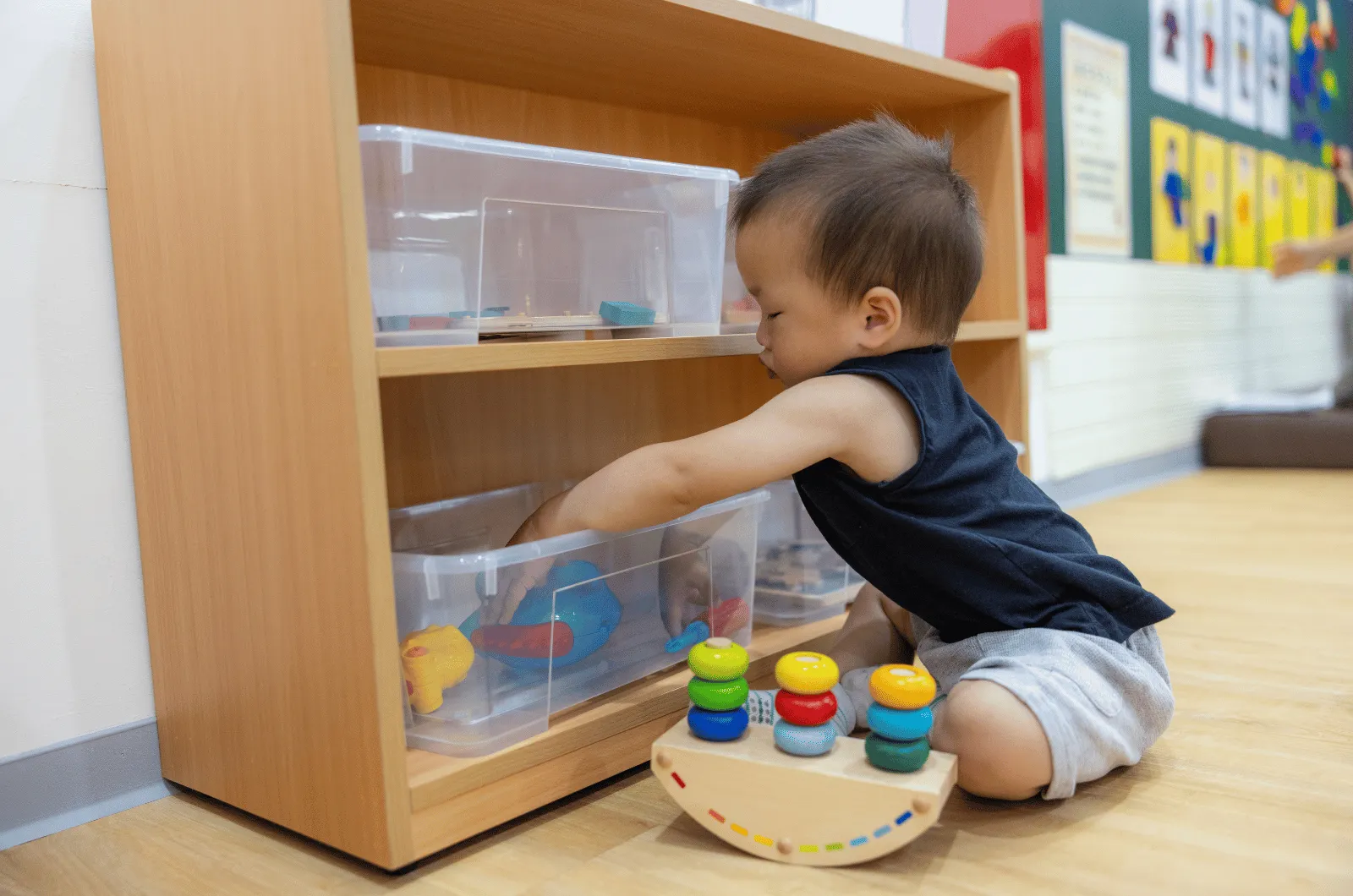 Preschooler sitting in front of a low wooden shelf, choosing a puzzle