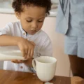 The pros and cons of Montessori in one moment: a toddler pours milk from a jug into a mug, spilling a little, while a parent stands close by