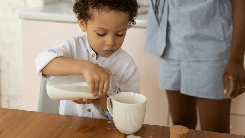 The pros and cons of Montessori in one moment: a toddler pours milk from a jug into a mug, spilling a little, while a parent stands close by