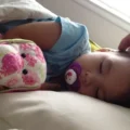 Toddler asleep with a pacifier and stuffed toys, a parent's hand near their head: sick day activities for toddlers