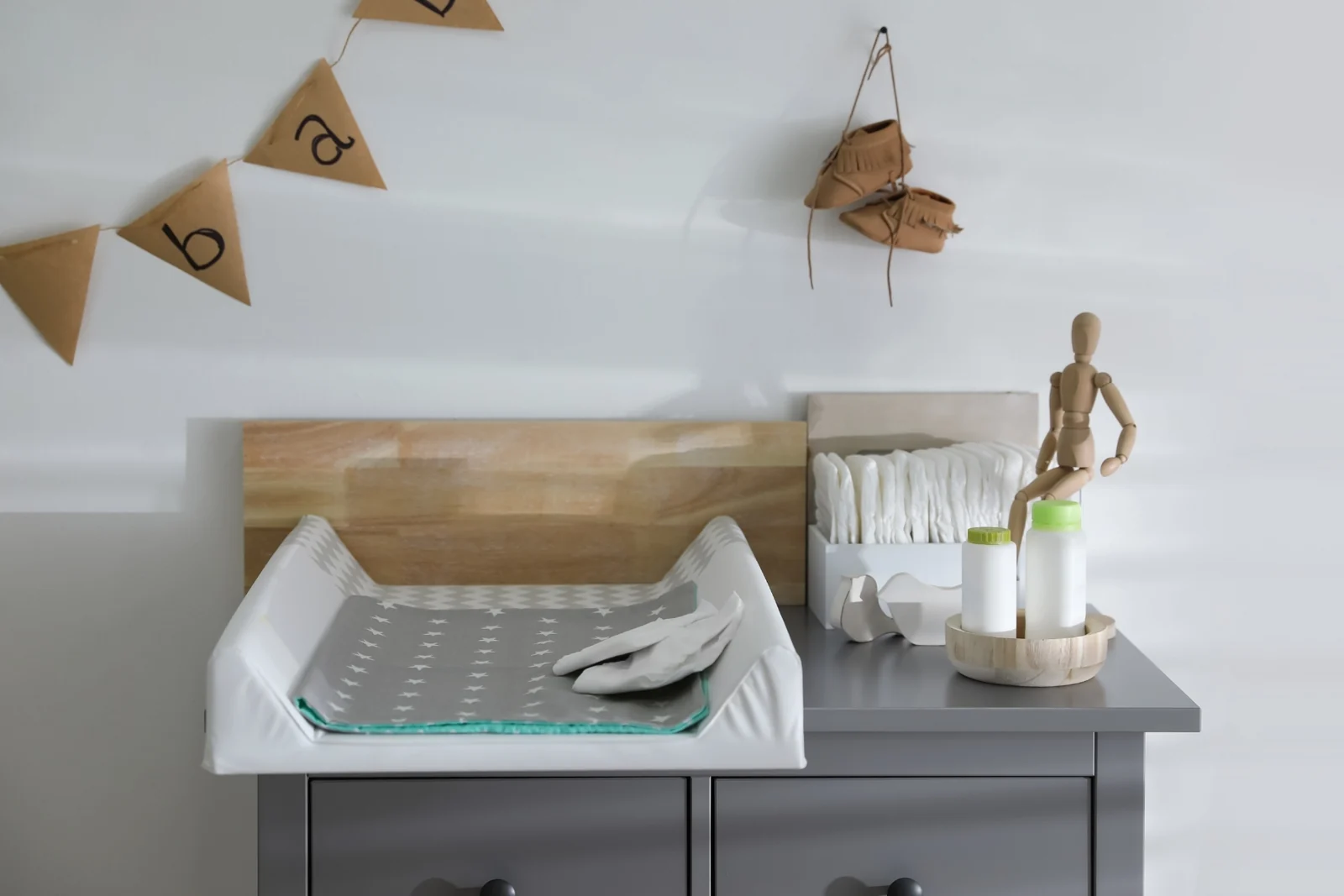 Changing pad on a gray dresser with a stack of diapers and two small bottles in a wooden tray