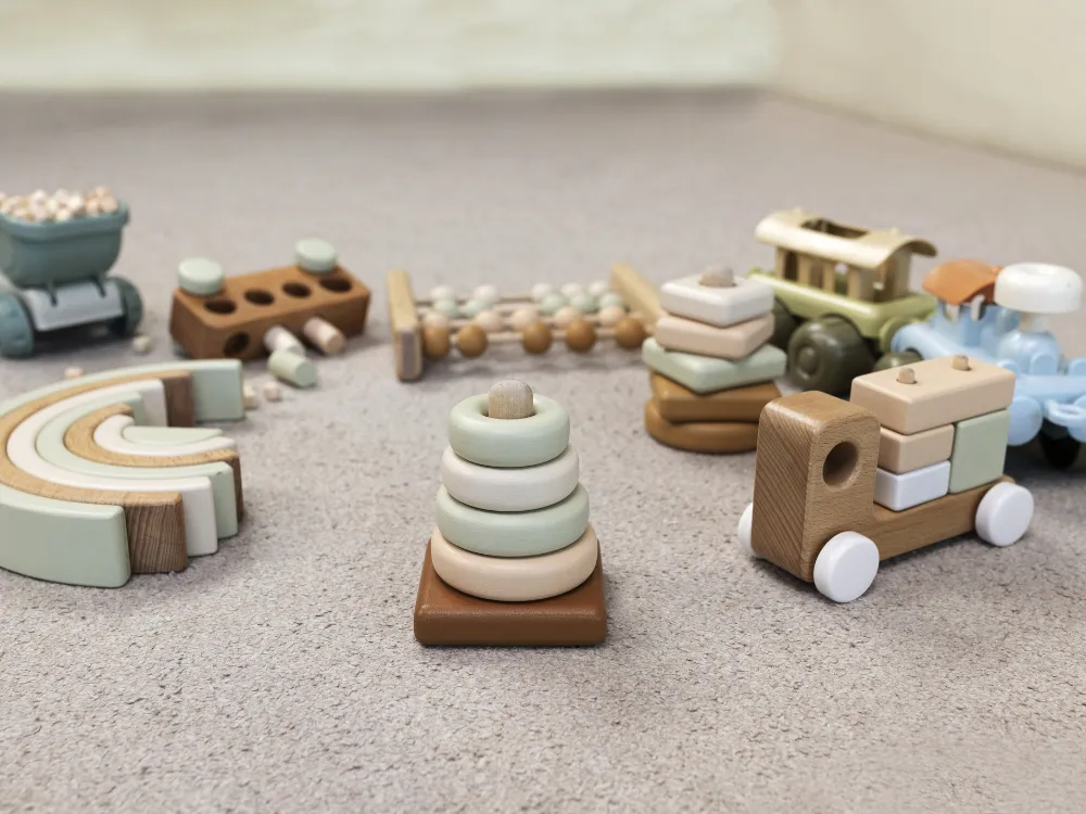 Simple wooden toys, including a ring stacker, a rainbow stacker and a toy truck, spread out on a carpet