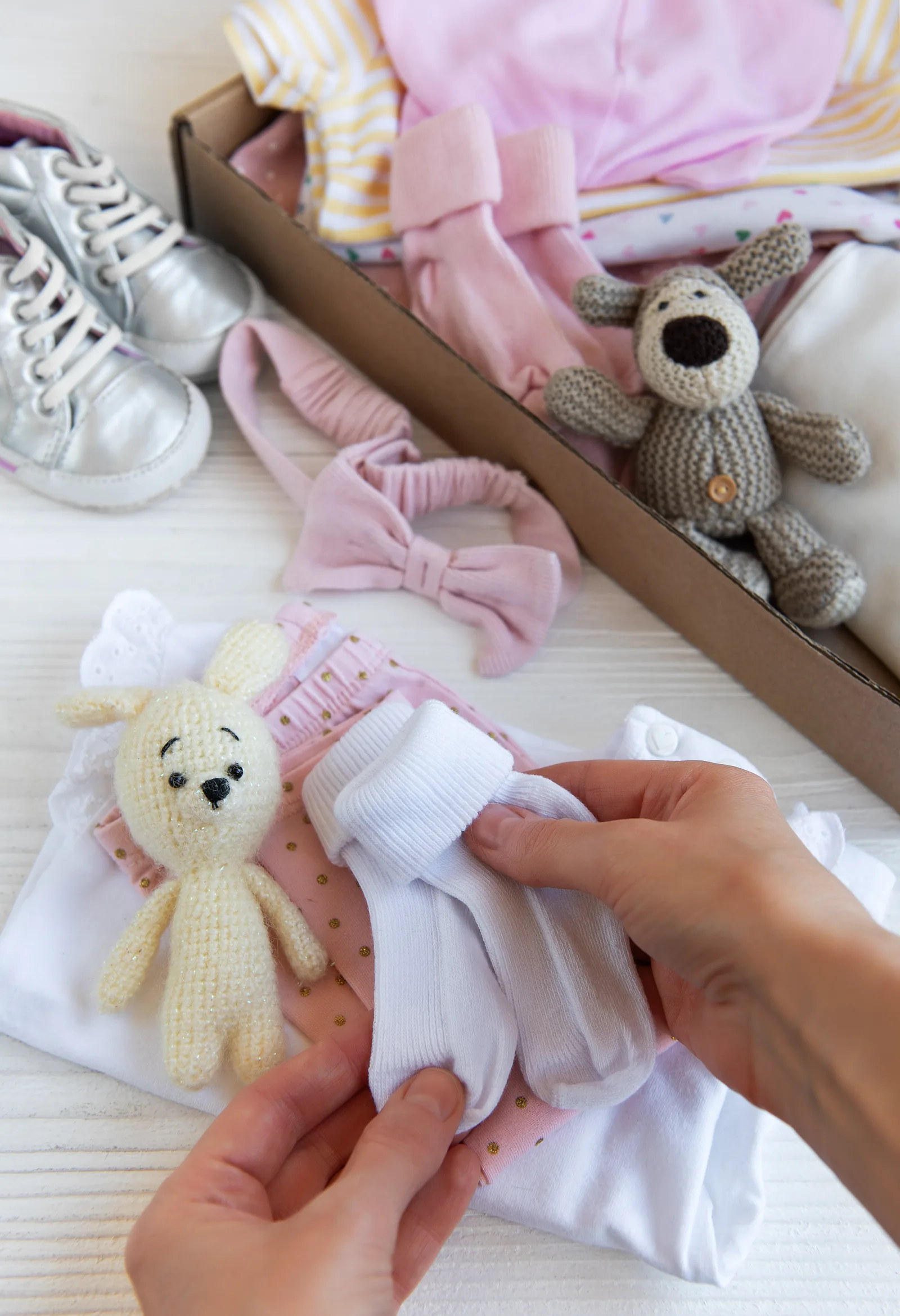 An adult's hands sort through a box of secondhand baby clothes and toys on a table