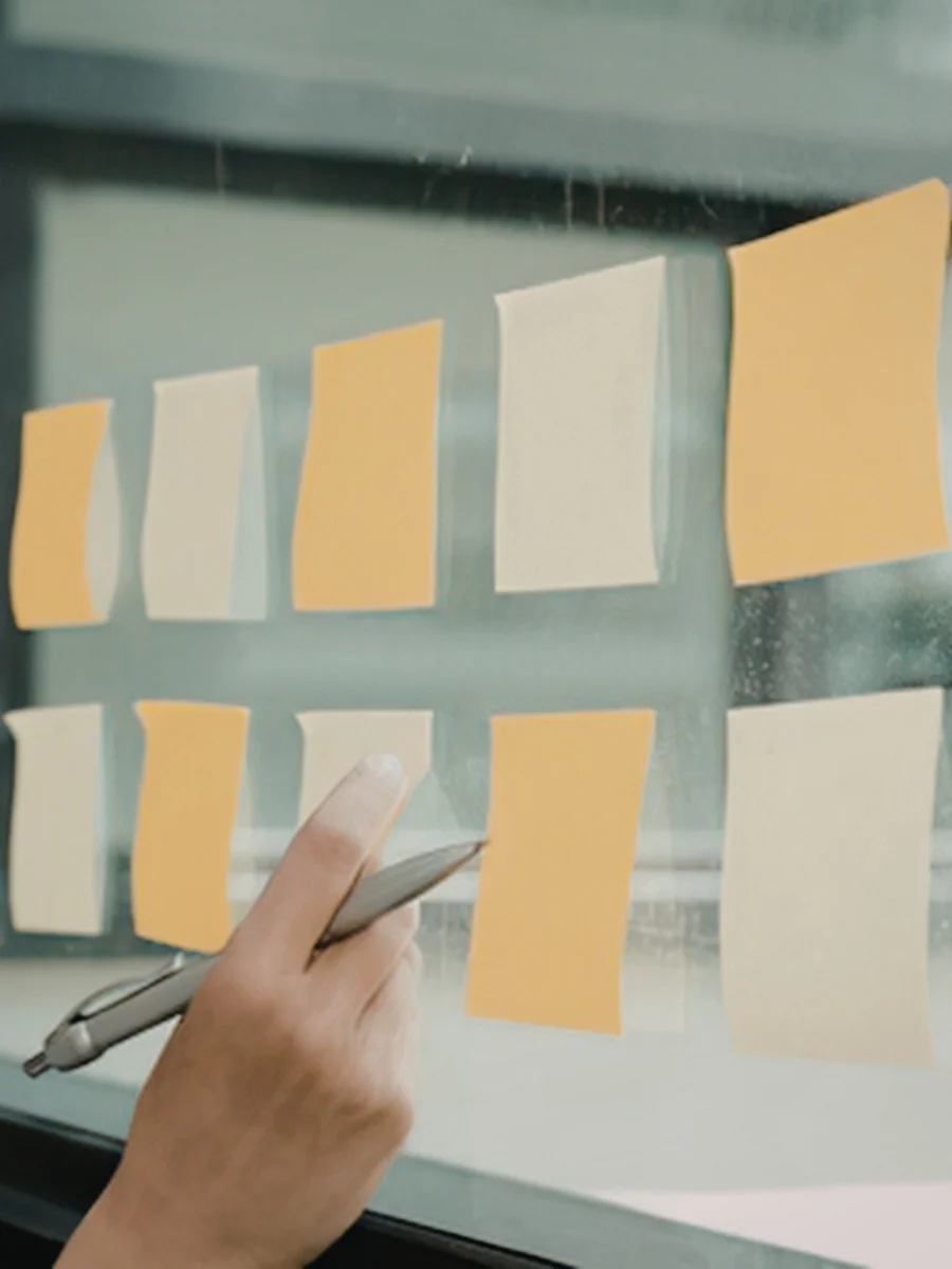 Hand holding a pen beside two rows of orange and cream sticky notes stuck on a window