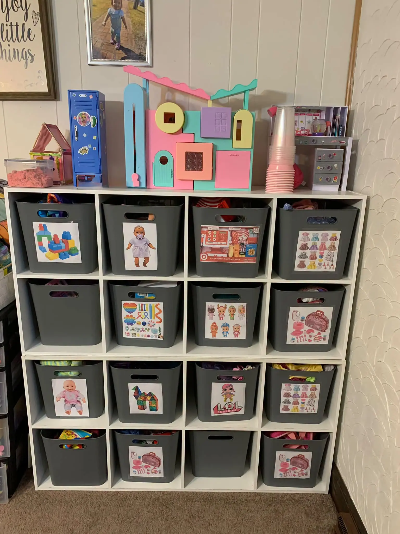 A white cube shelf with gray storage bins, each labeled with a picture of the toys inside