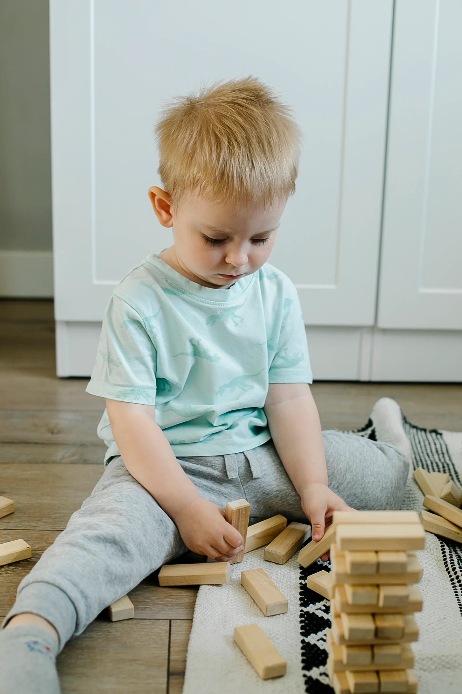 Toddler sitting on a rug, completely absorbed in stacking wooden blocks into a tower