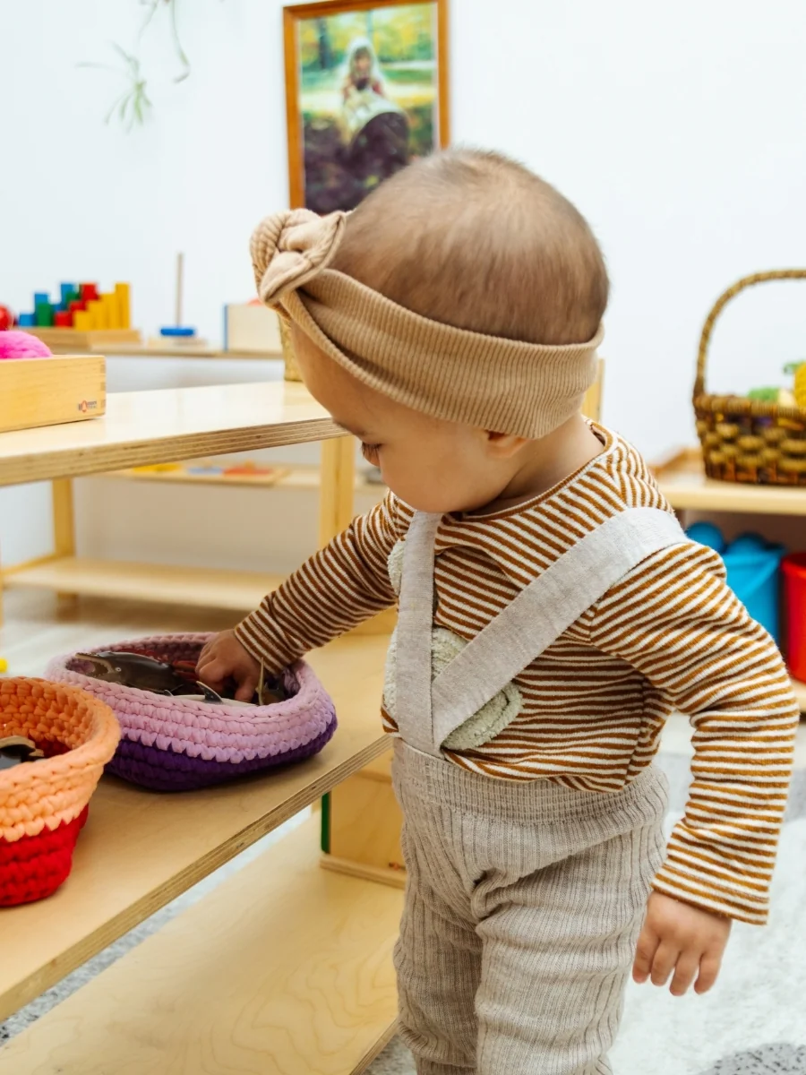 A toddler reaches for a toy on a low wooden shelf at their own height