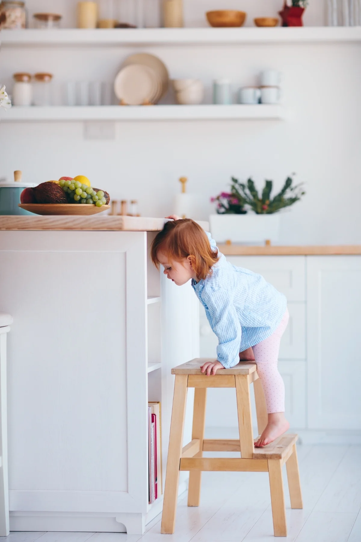 A toddler stepping up onto a small wooden step stool beside a kitchen island