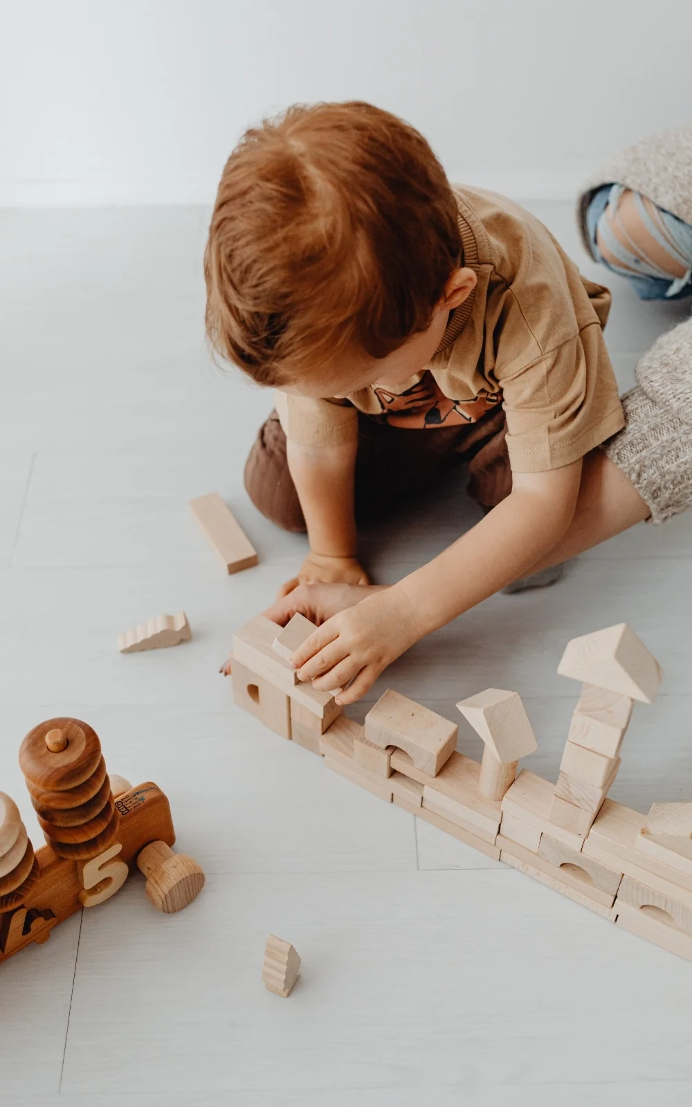 A toddler sits on the floor, concentrating hard on stacking wooden blocks