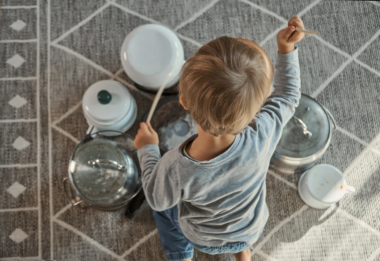 A toddler on a rug drums on kitchen pots and lids, seen from above