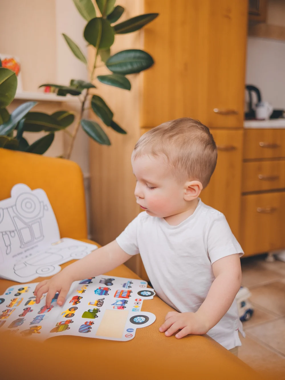 Toddler in a white T-shirt leaning over a sheet of vehicle stickers and touching one with a finger