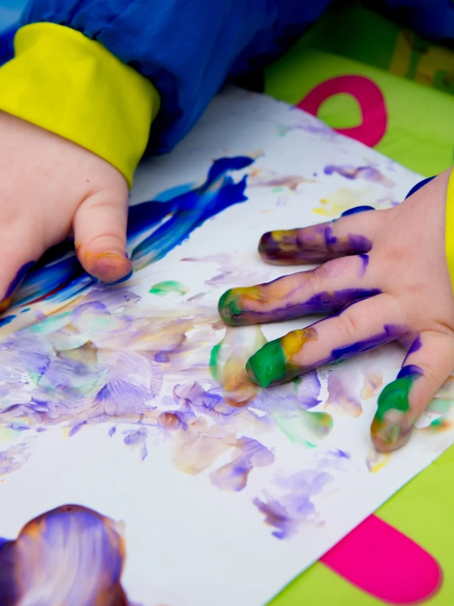 Two small hands with paint-covered fingers pressing onto a big sheet of paper