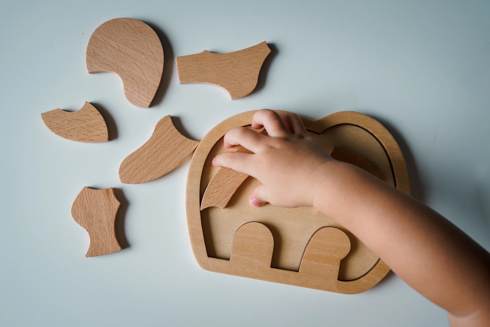 A toddler fits a large wooden shape into a puzzle board on the floor