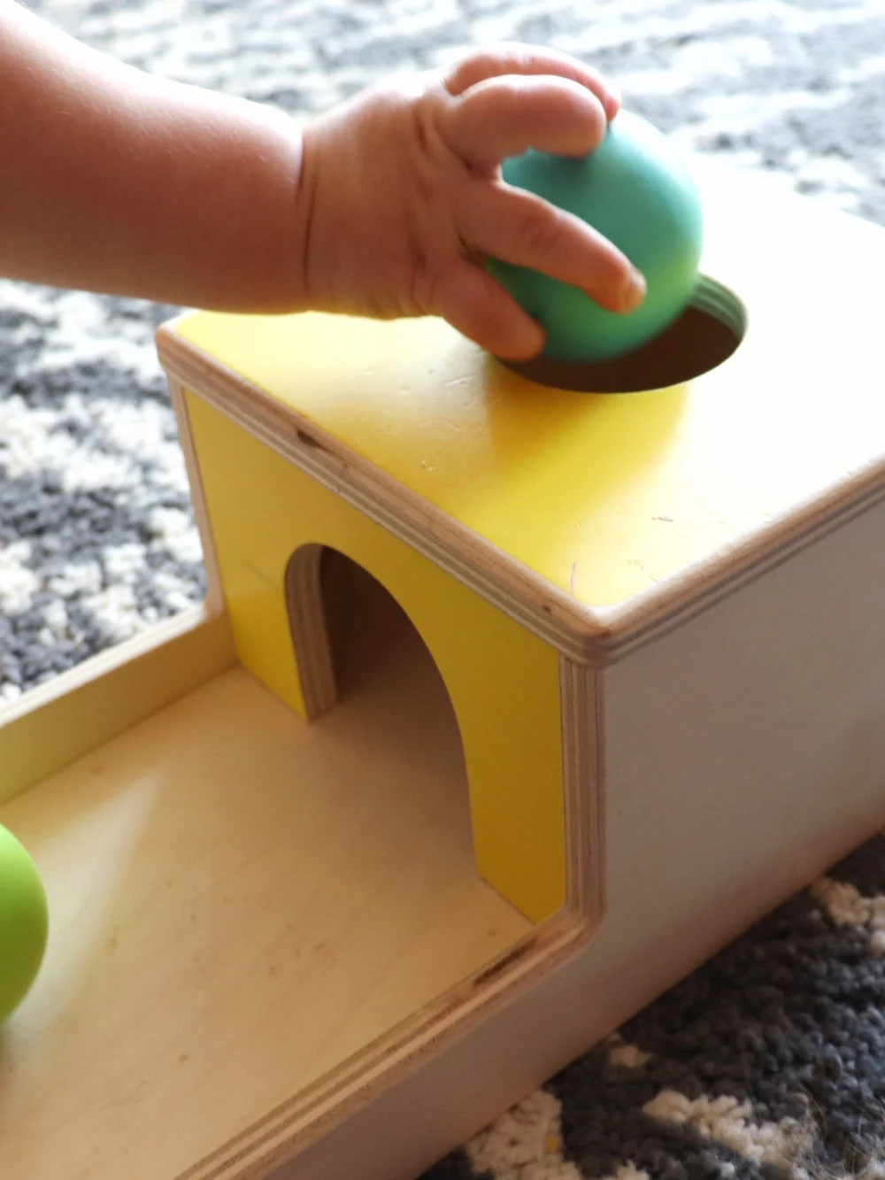 Close-up of a toddler's hand dropping a green wooden ball through the round hole of a wooden box
