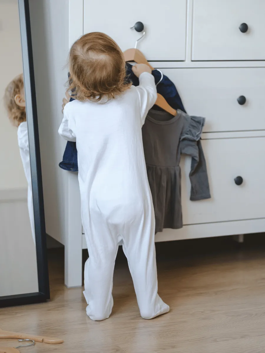 Toddler reaching up to hang a small coat on a low wall hook near the front door