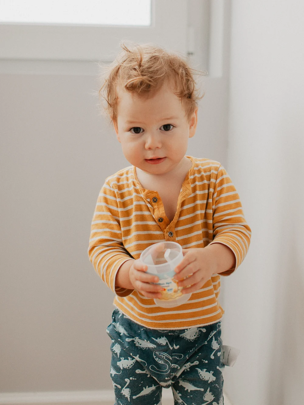 Toddler walking slowly across a kitchen floor, carrying a very full cup of milk with both hands