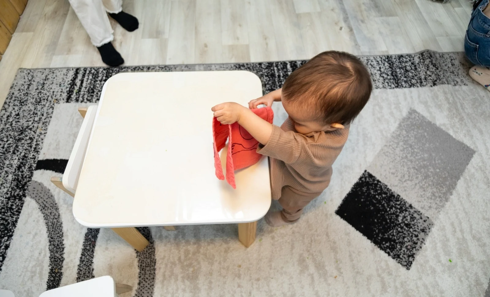 Toddler standing at a small white table holding up a red cloth