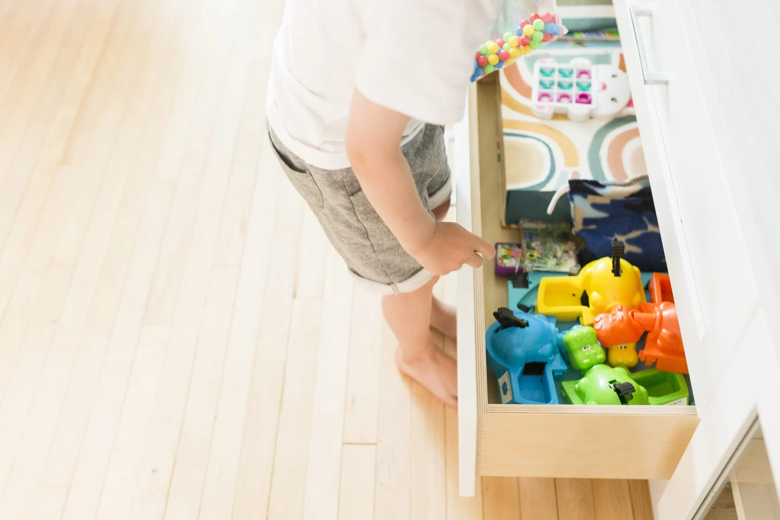 A toddler pulls a toy bin out of a low storage unit