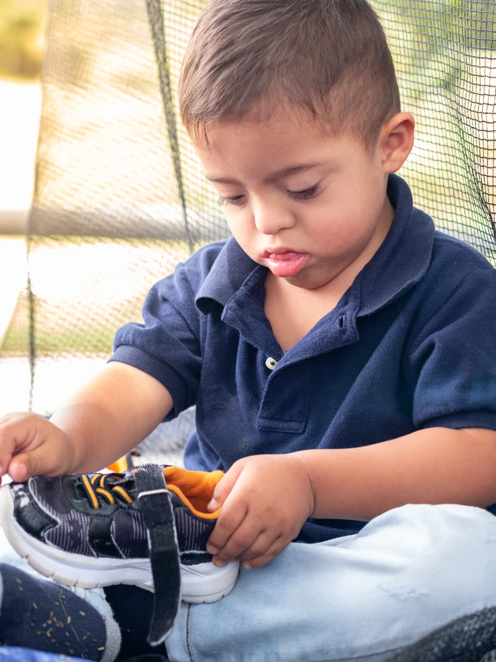 Toddler sitting down, working hard to pull on a sneaker without help