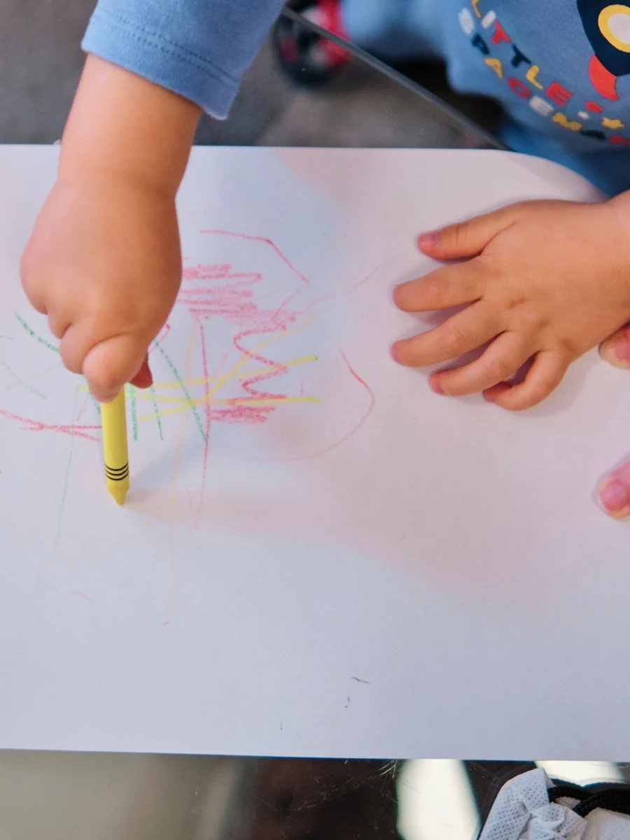 Toddler's hands scribbling with a yellow crayon on a sheet of white paper