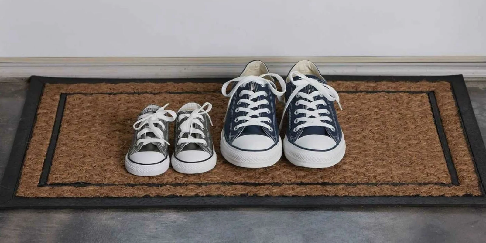 Small sneakers lined up beside a pair of adult sneakers on a doormat