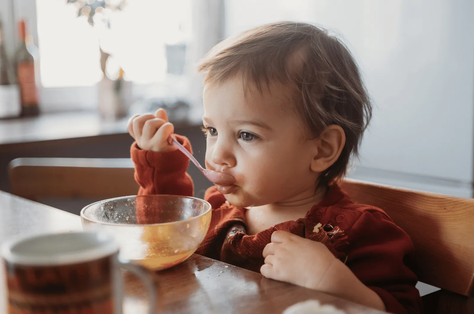 Toddler sitting at a low table trying to feed themselves with a spoon from a small bowl