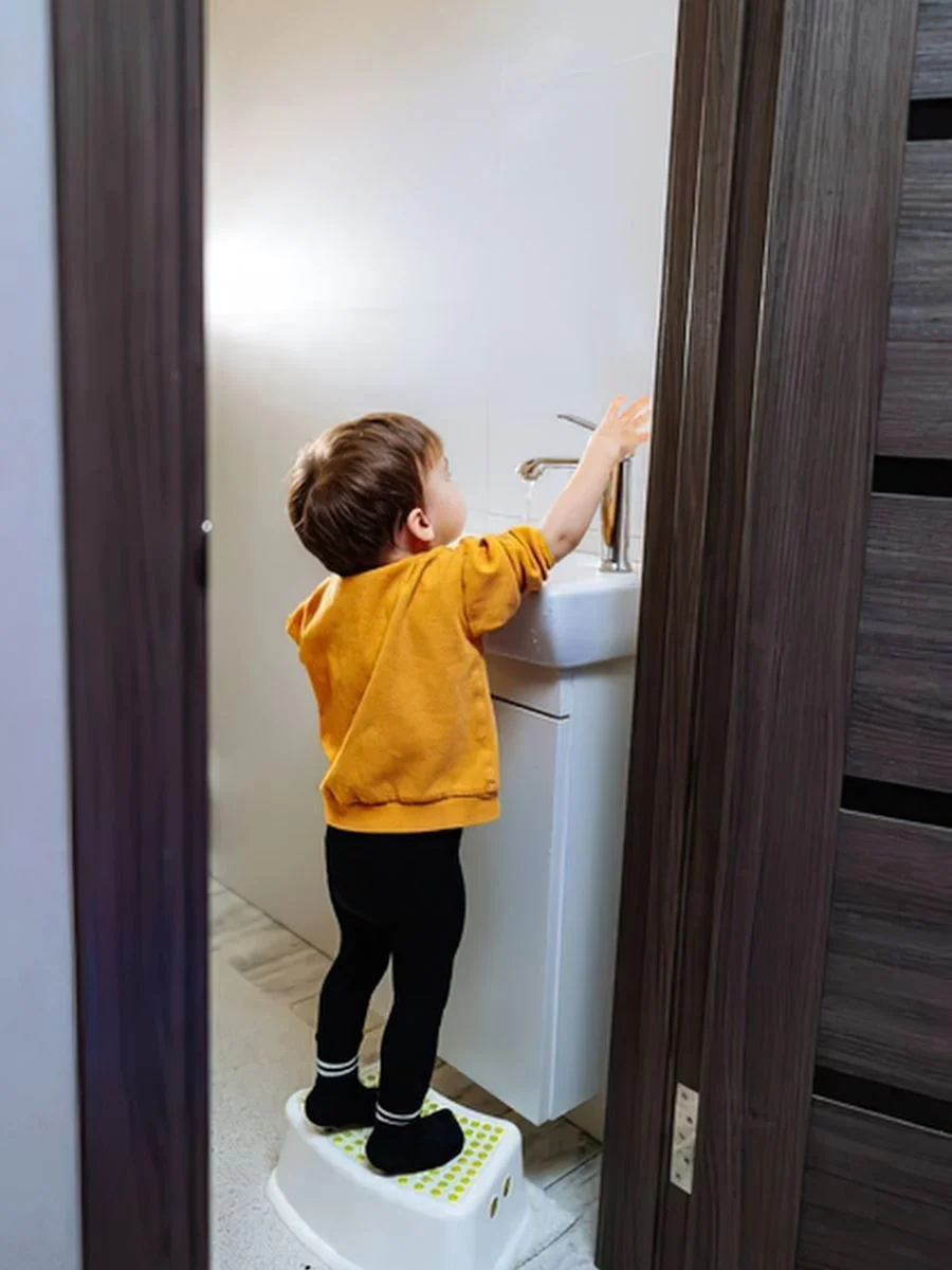 Toddler standing on a sturdy step stool at the bathroom sink, washing their hands