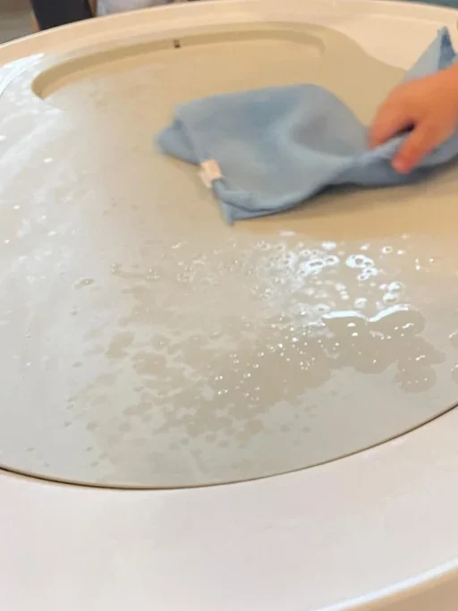 A toddler's hand wiping a foamy white tray with a small blue cloth