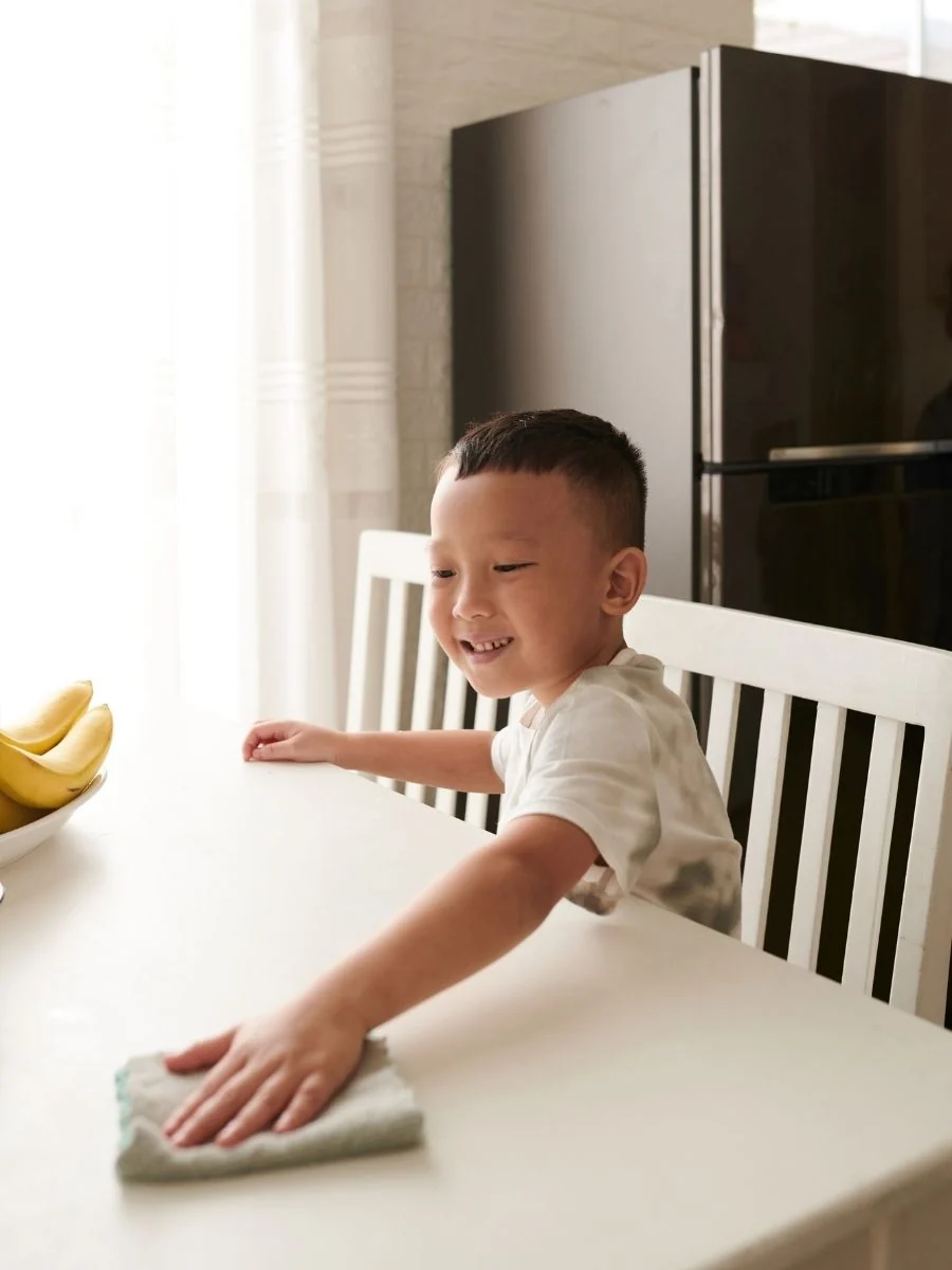 Toddler wiping a table with a small cloth
